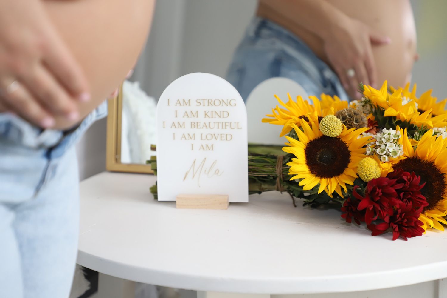 Maternity affirmation sign displayed beside sunflowers and a mirror