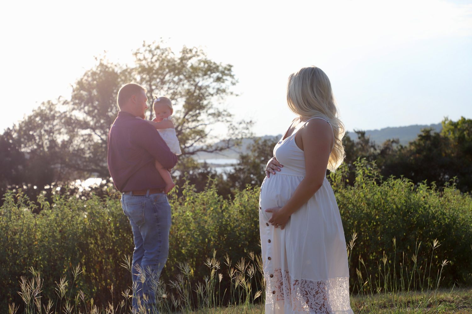 Expectant mother watching the father hold their baby at sunset