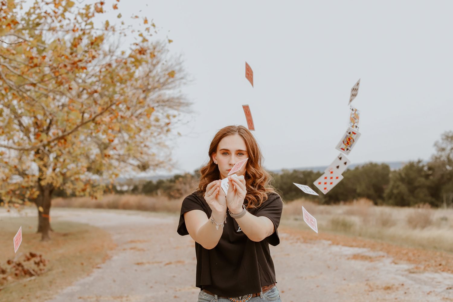 Red-haired senior posing outdoors with playing cards floating around her