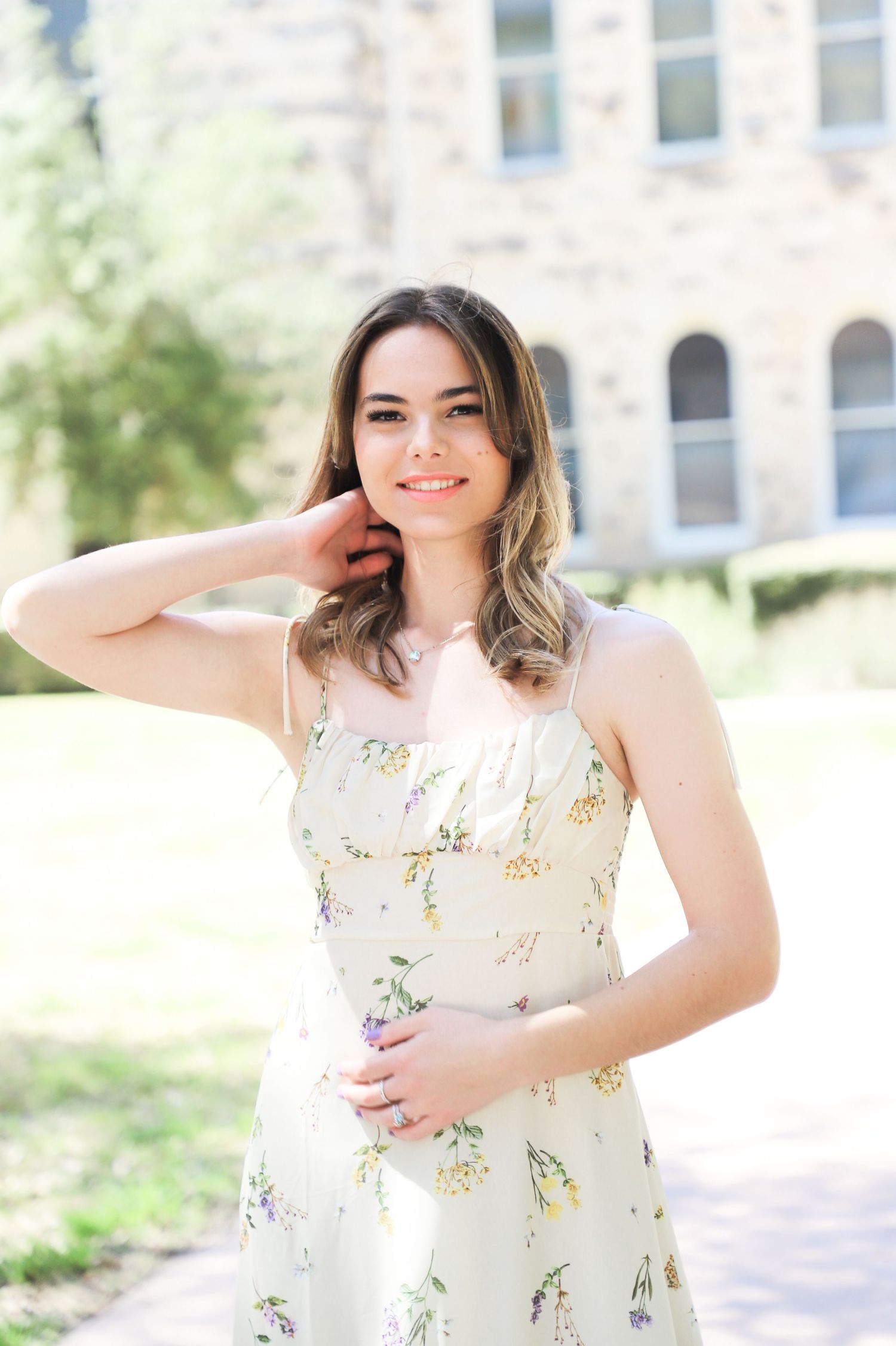 Senior in a floral dress posing in front of a historic stone building