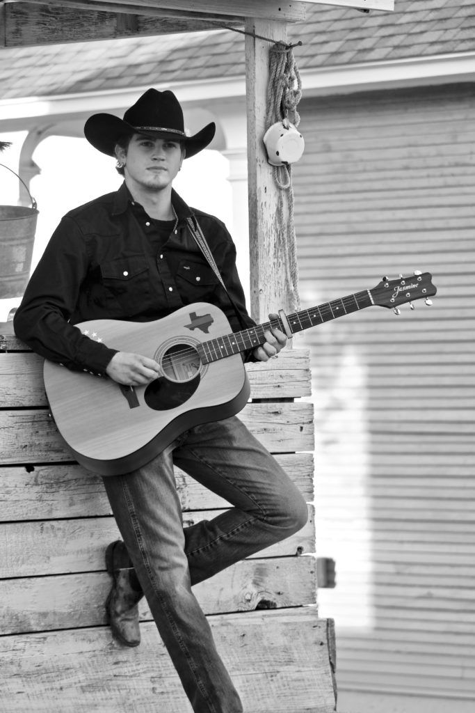 Black-and-white senior portrait with a cowboy hat and acoustic guitar