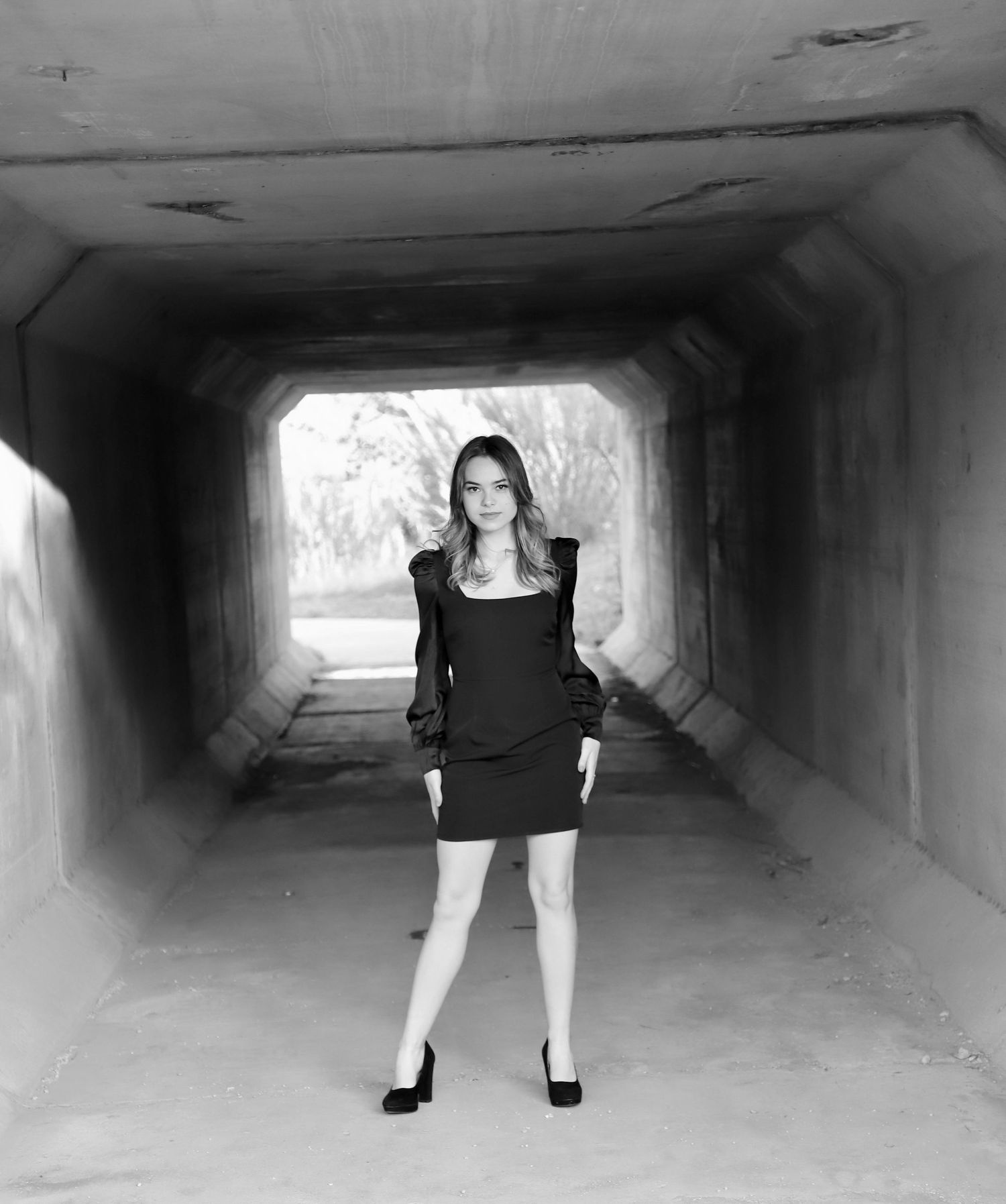 Black-and-white senior portrait in a black dress inside a concrete tunnel