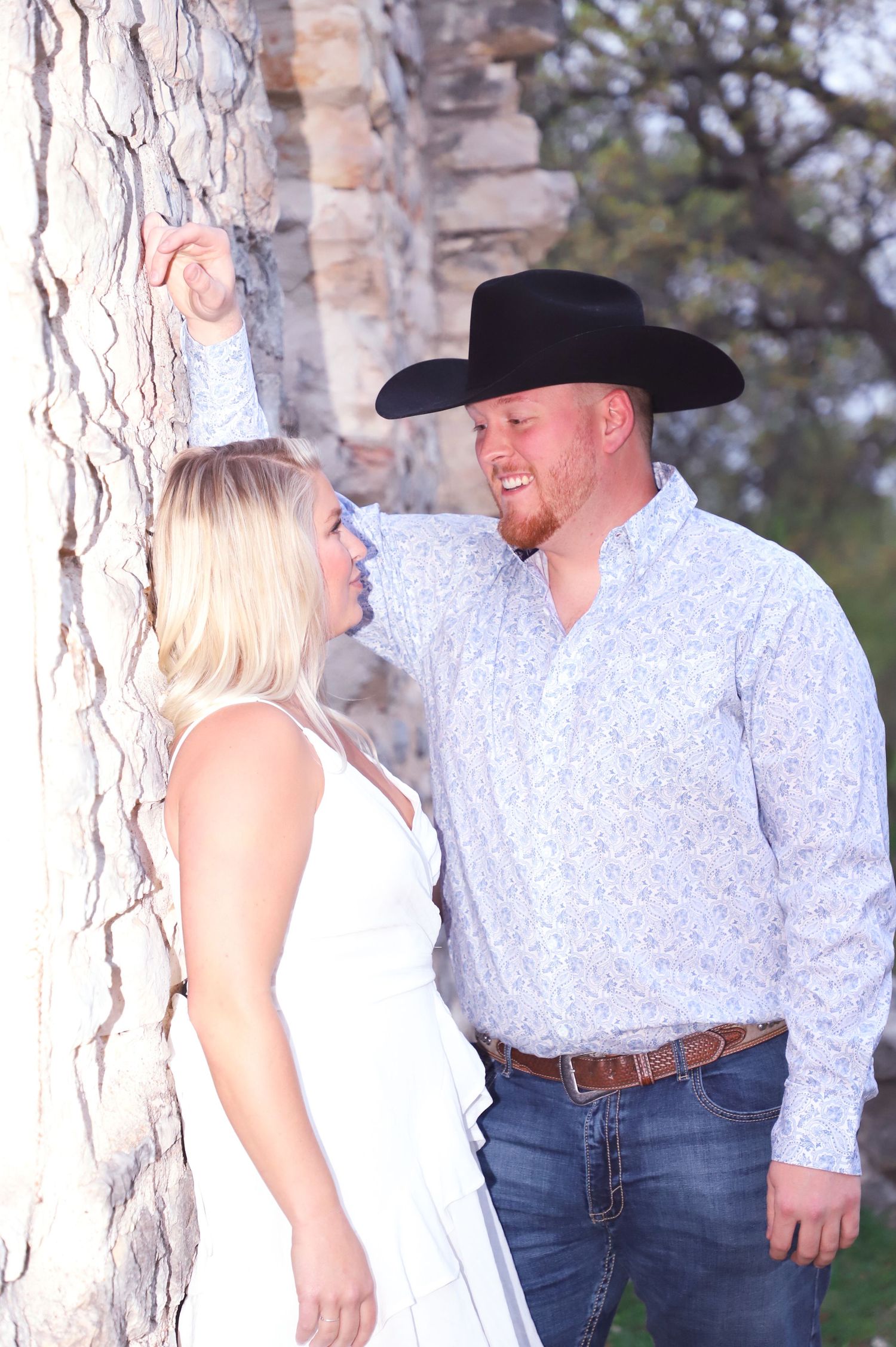 Couple in western attire smiling together beside a large tree