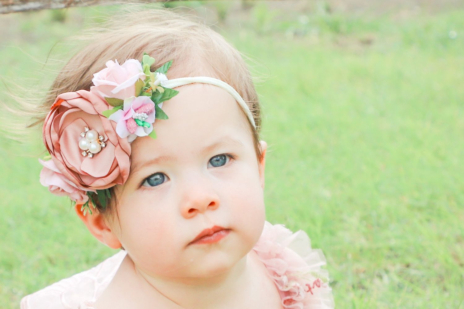 Baby girl wearing a pink floral headband while sitting in the grass