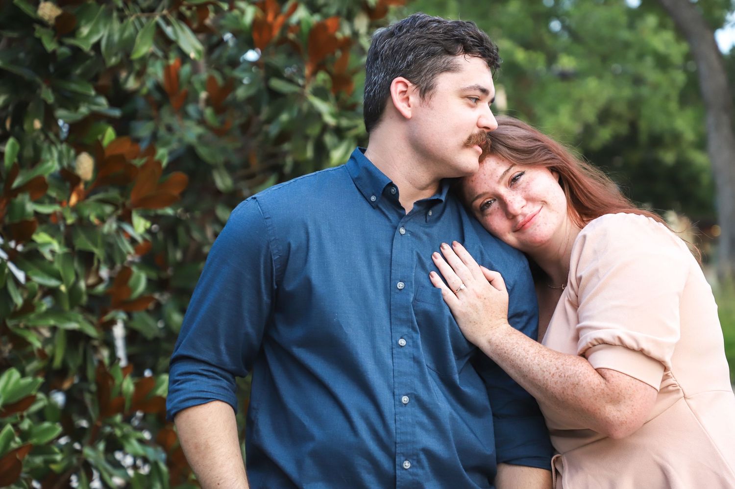 Engaged couple embracing beneath a magnolia tree