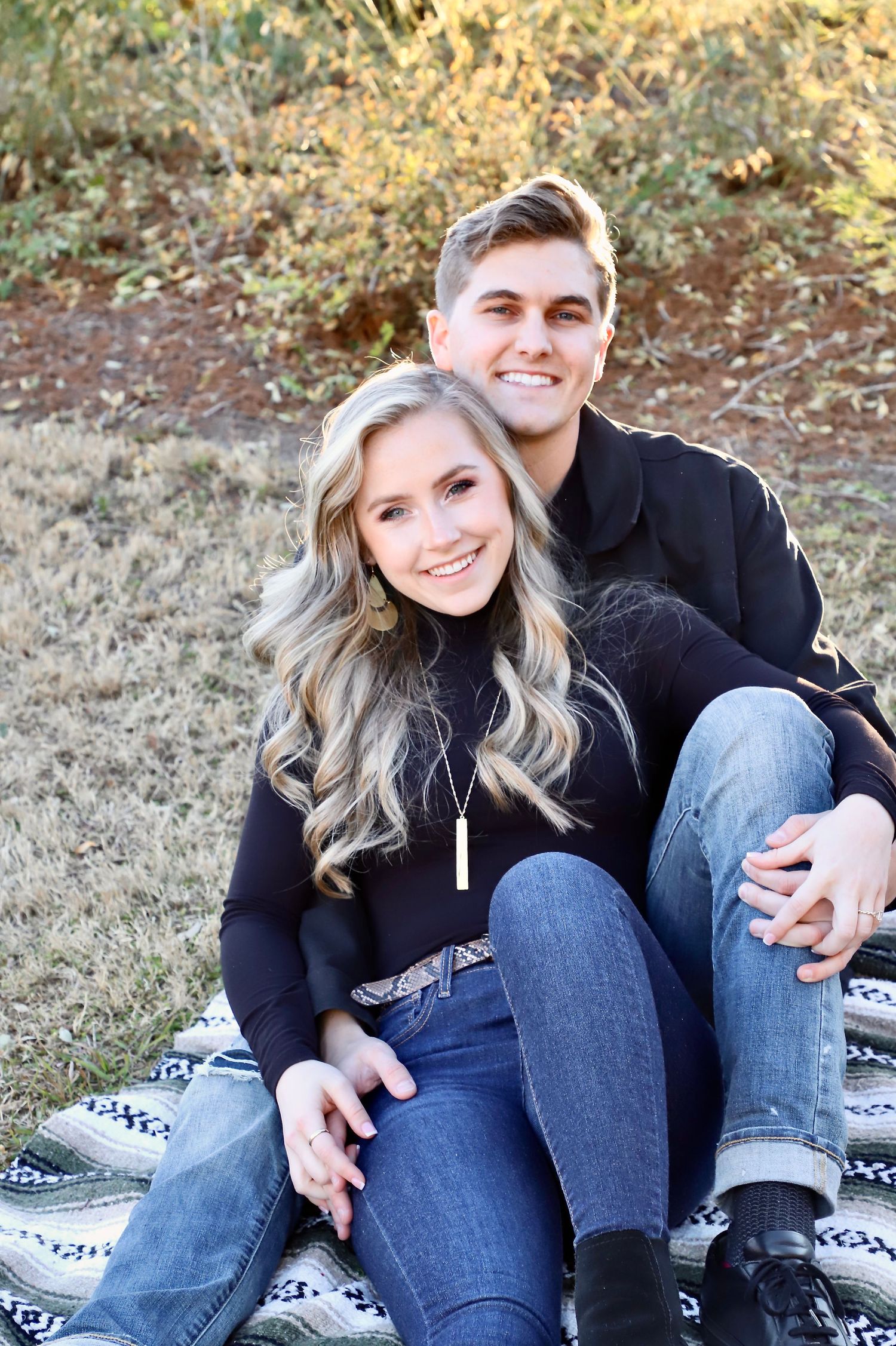 Smiling engaged couple seated together on an outdoor blanket