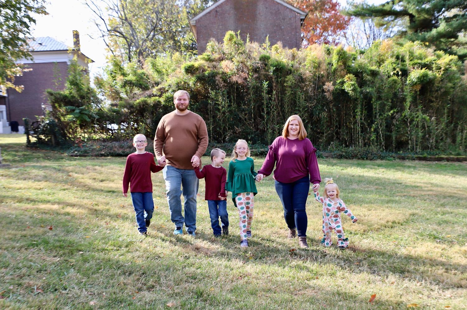 Family of six walking hand in hand across a grassy lawn