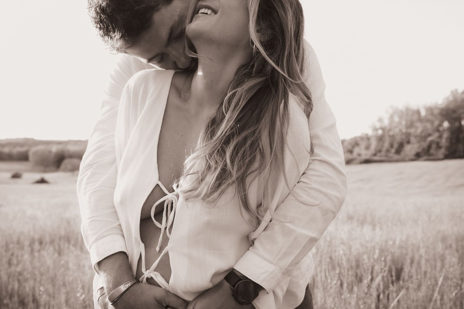 Gros plan intimiste d'un futur papa enlaçant une femme enceinte dans un champ, photographie de couple naturelle et chaleureuse.