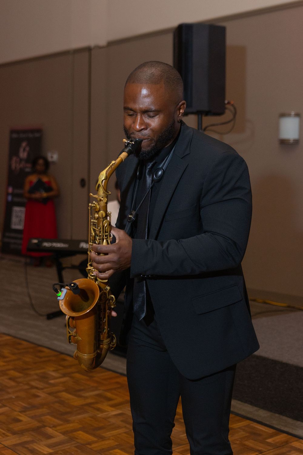 Saxophonist in formal attire performs passionately during an indoor event.