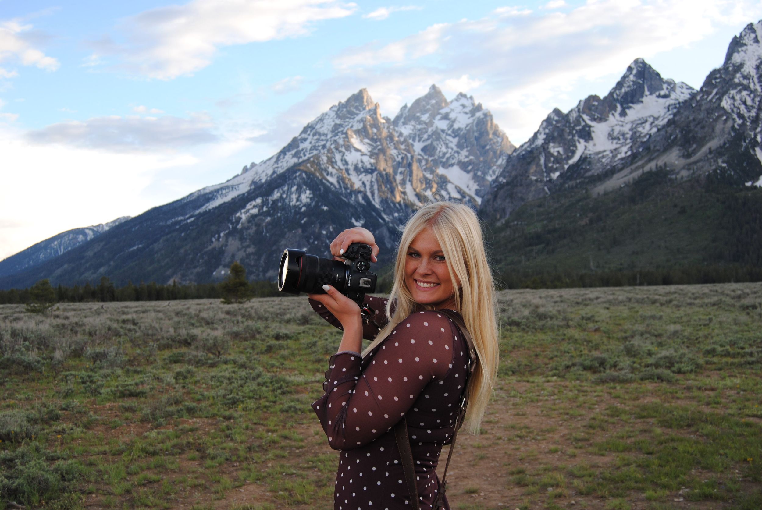 Person in black clothing laughs joyfully in a mountain field during golden hour.