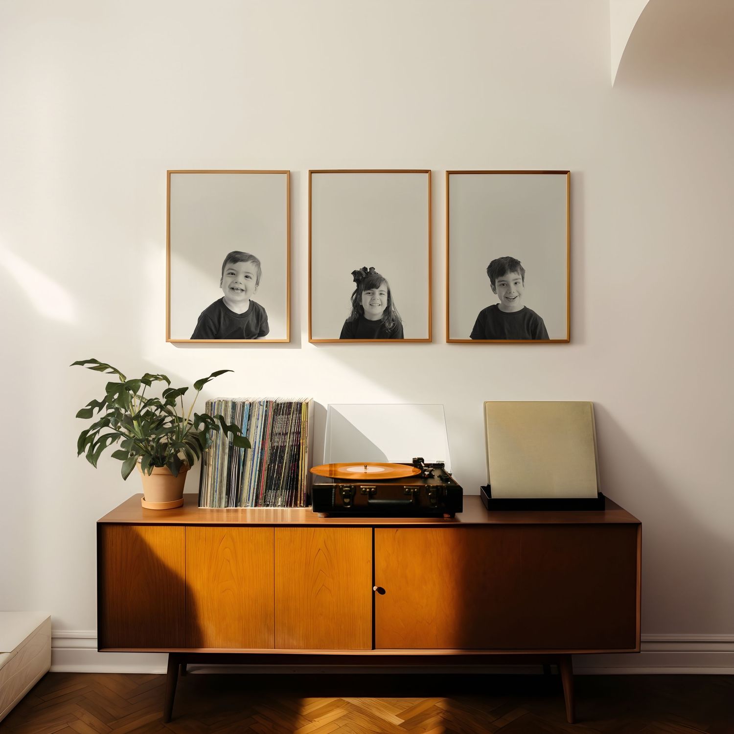 Mid-century modern credenza with potted plant, record collection, and three framed portraits on white wall above.