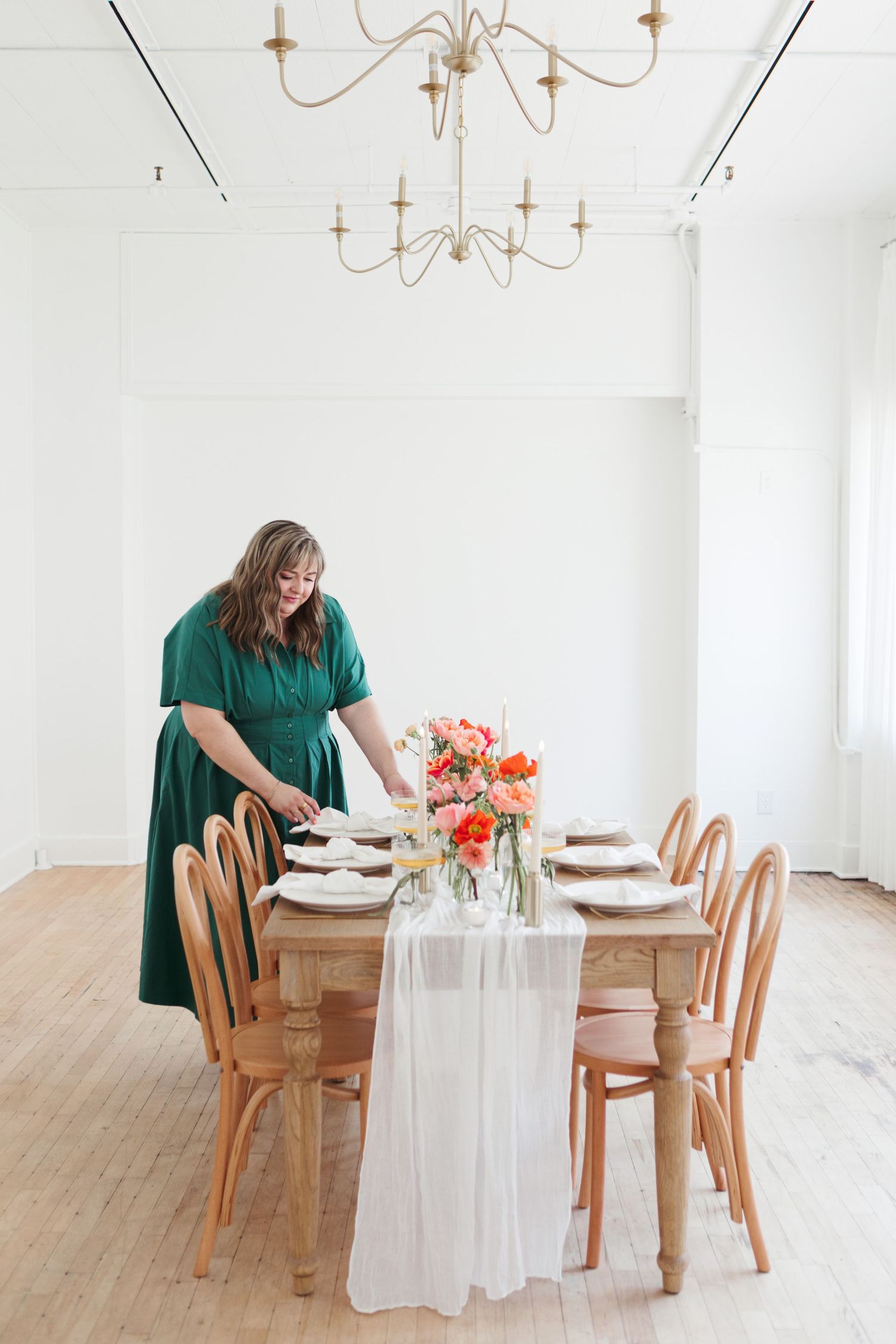 A dining table setup with wooden chairs, white tablecloth, and bright floral centerpiece under elegant chandeliers.