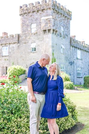 Couple in front of Irish castle, smiling looking at eachother.