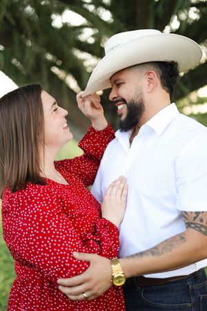 Couple tipping cowboy hat under tree during golden hour.