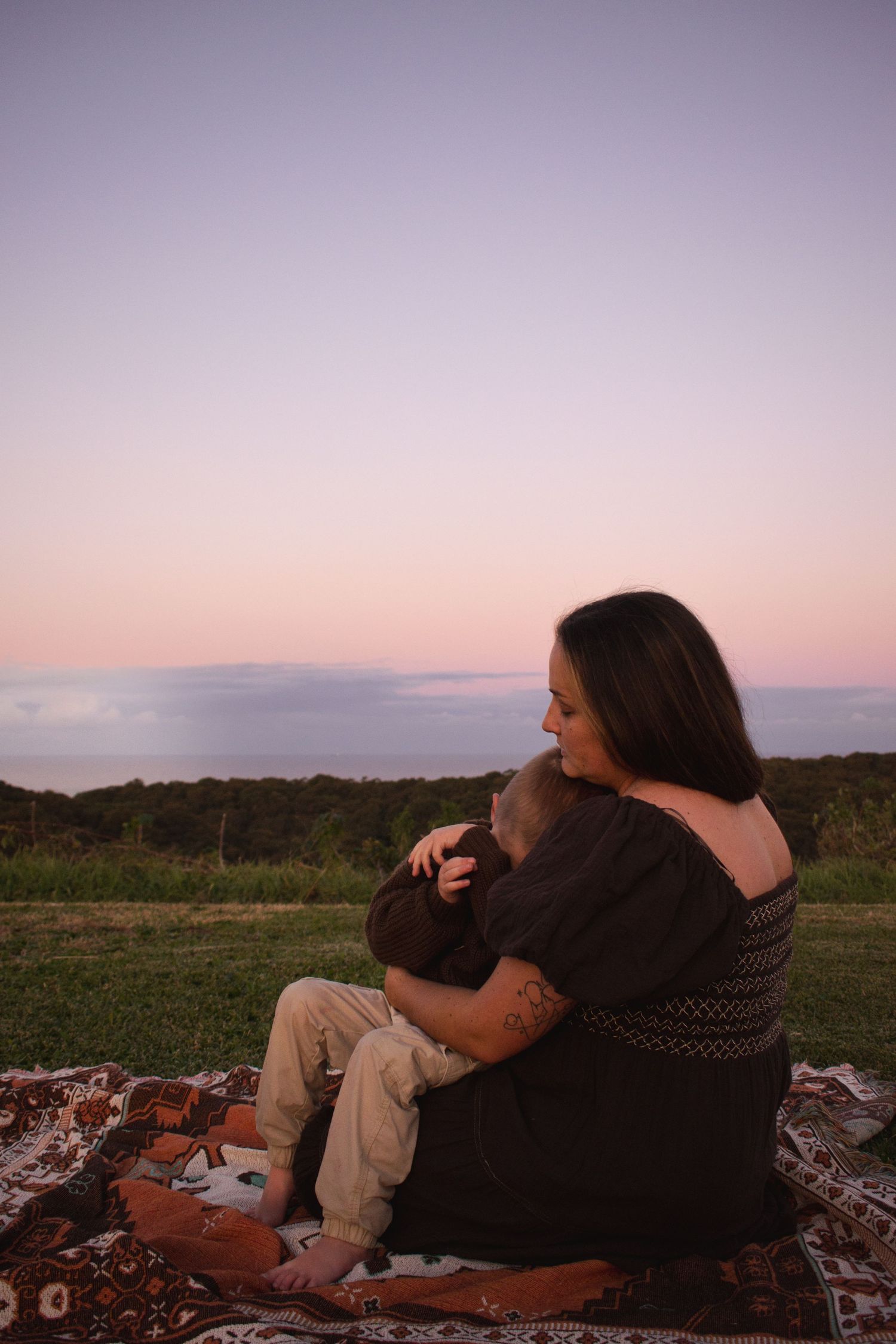 Mother holds her preschool child close providing comfort during a sunset motherhood photoshoot at Whitebridge Lookout Dudley Beach Newcastle