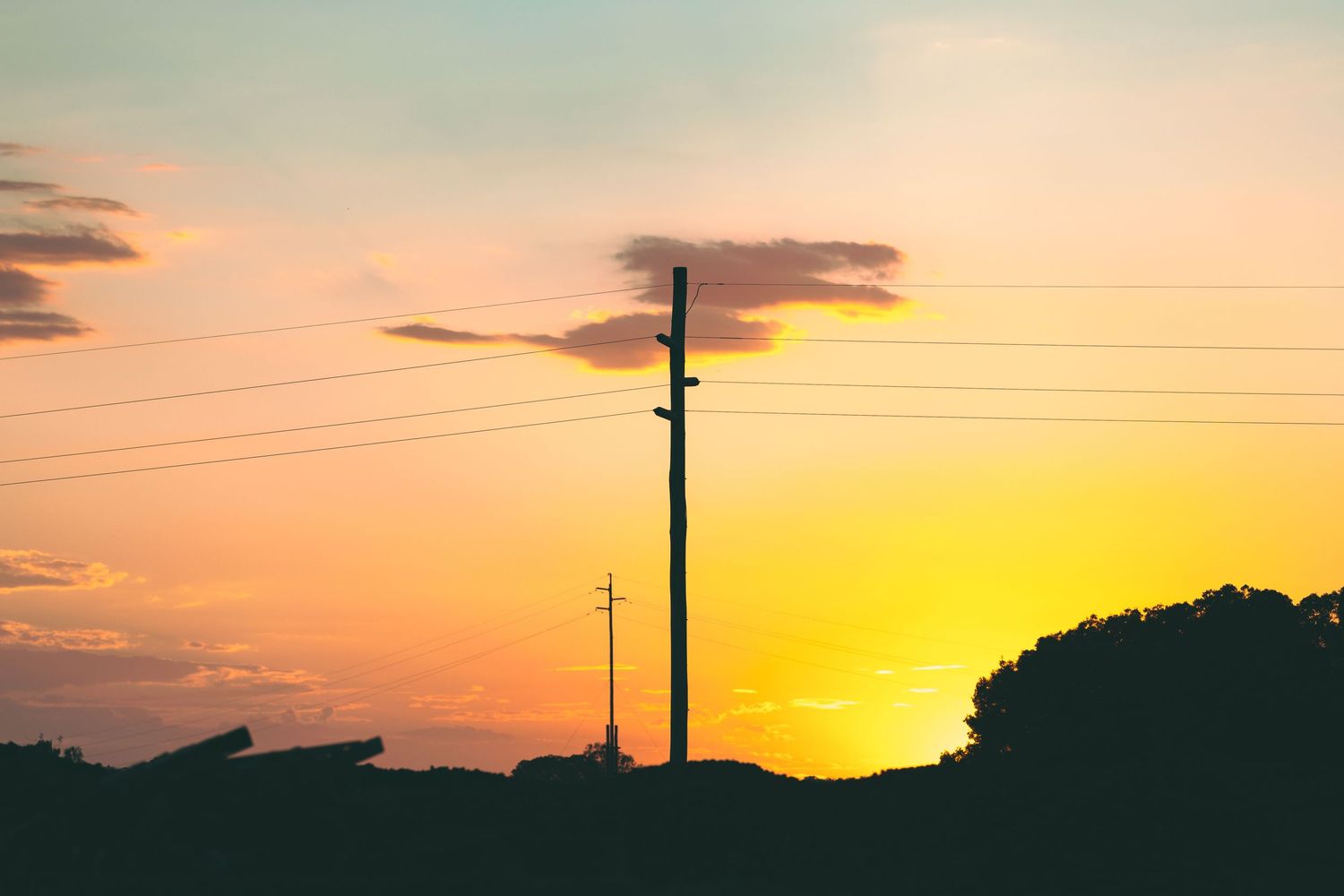 Silhouette of power lines and utility poles against a vibrant orange and yellow sunset sky.