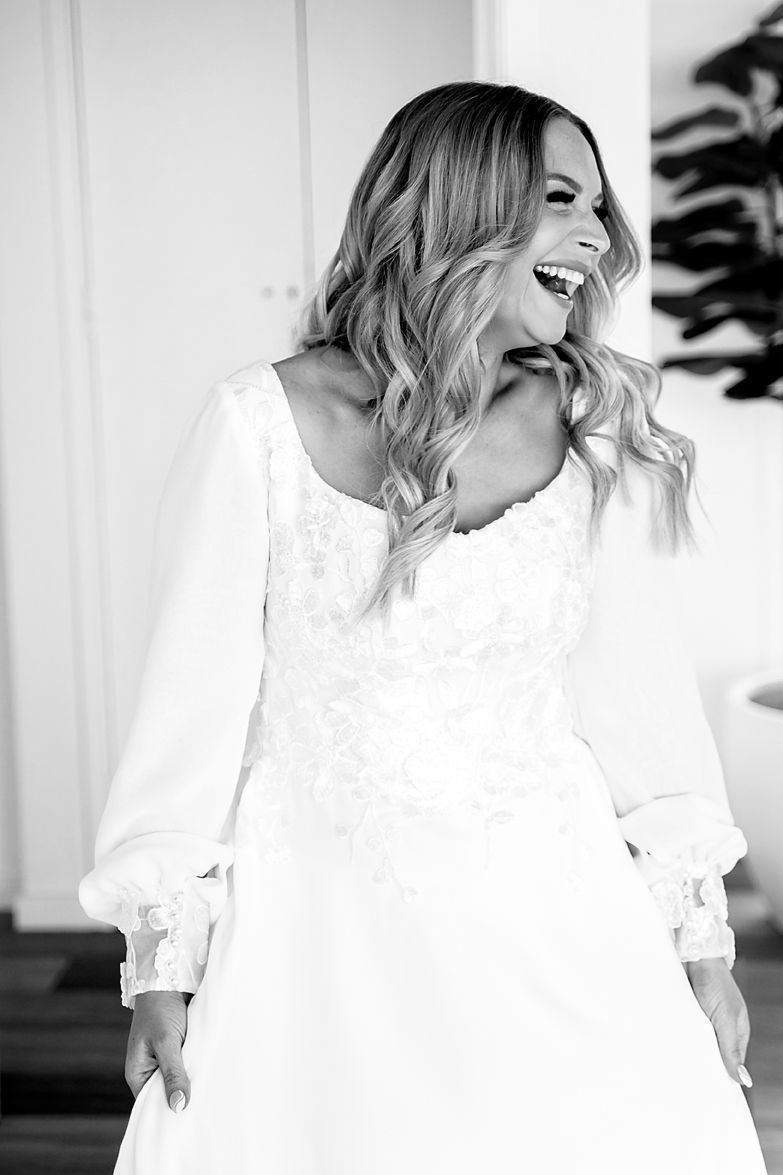 Black and white portrait of a person with wavy blonde hair wearing a white dress with lace details and billowy sleeves.