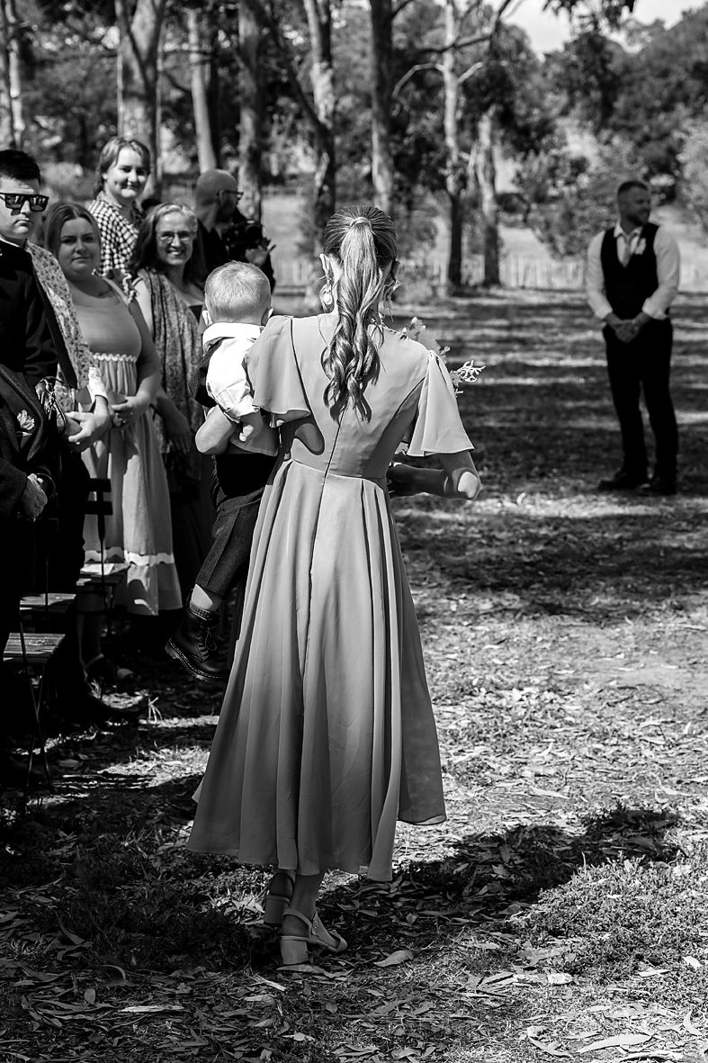 Black and white photograph showing people in vintage dresses standing outdoors in a park-like setting.