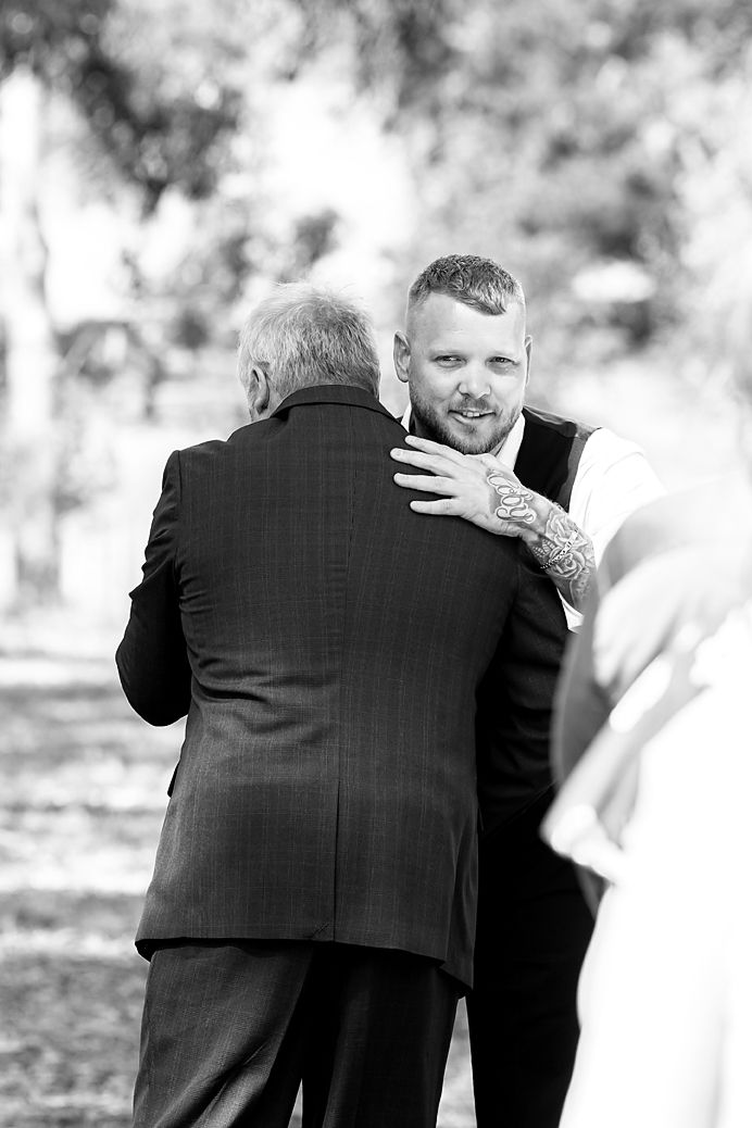 Black and white wedding photo showing an emotional embrace between figures in formal attire outdoors.