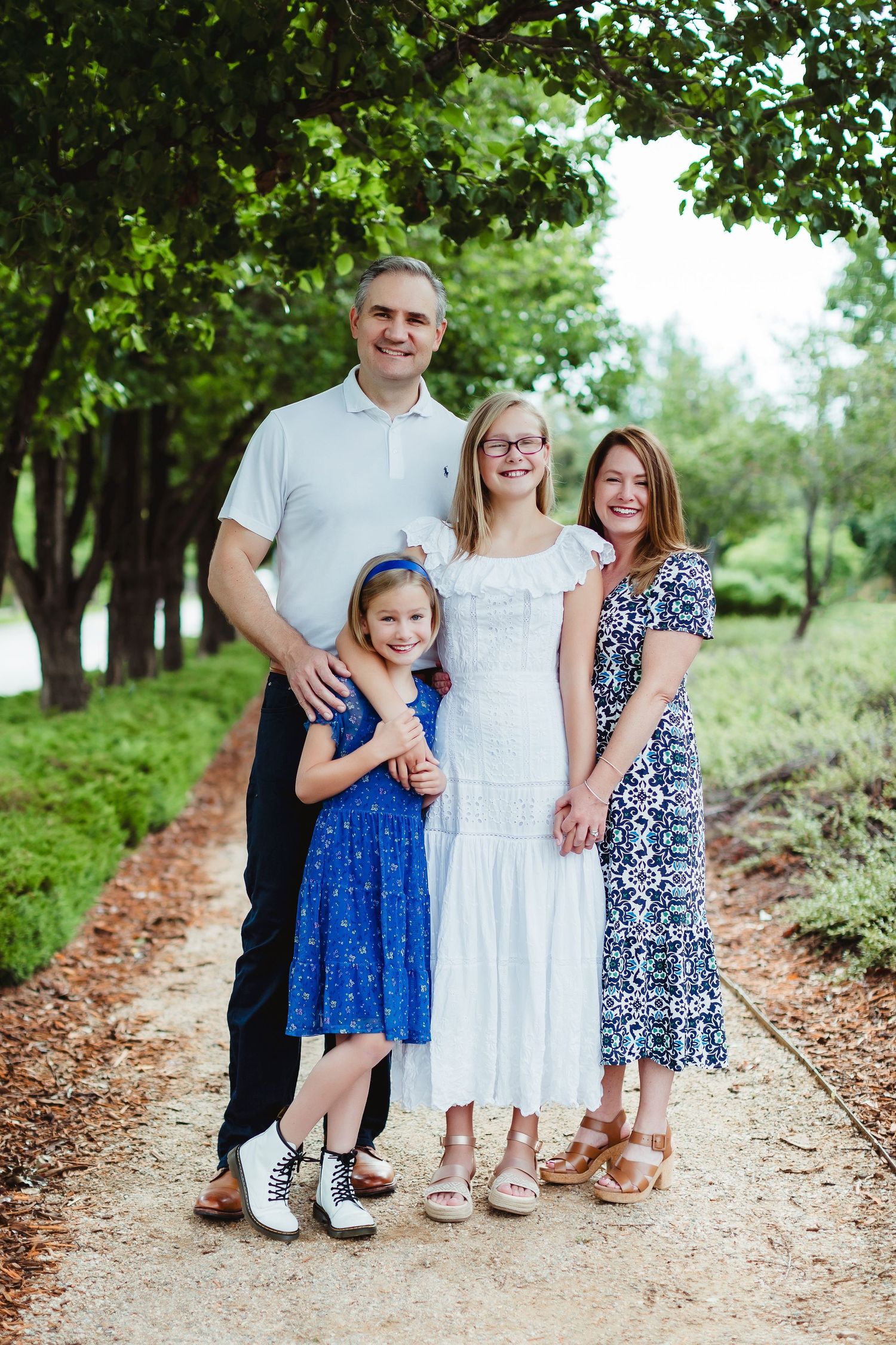 A family portrait session on a tree-lined path shows coordinated blue and white outfits.