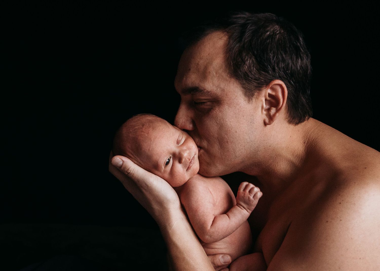 A tender moment between parent and newborn baby against dark background.