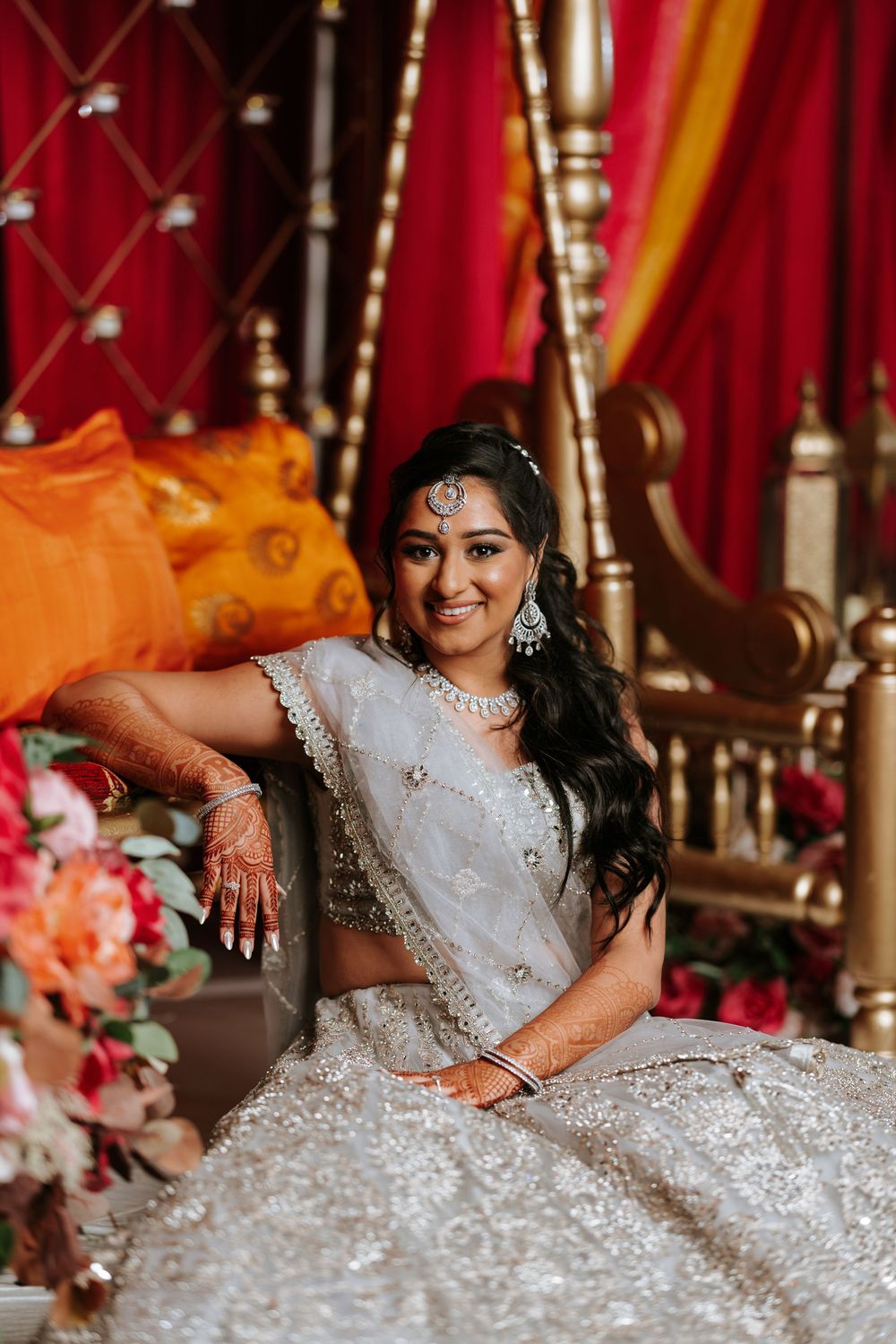 Bride in an embellished white gown reclines gracefully amidst traditional wedding decorations.