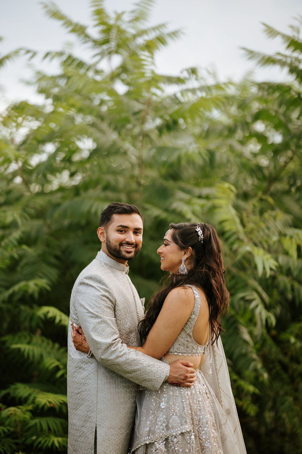 A romantic wedding portrait of a couple in elegant South Asian attire against a backdrop of ferns.