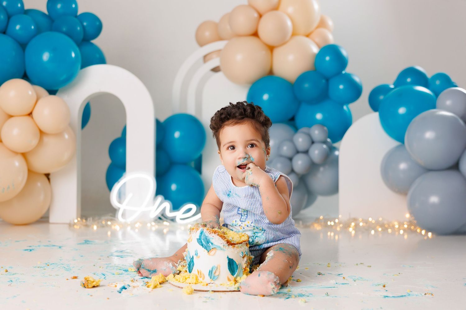 First birthday cake smash photoshoot with blue and peach balloon arch decorations and white number one prop.