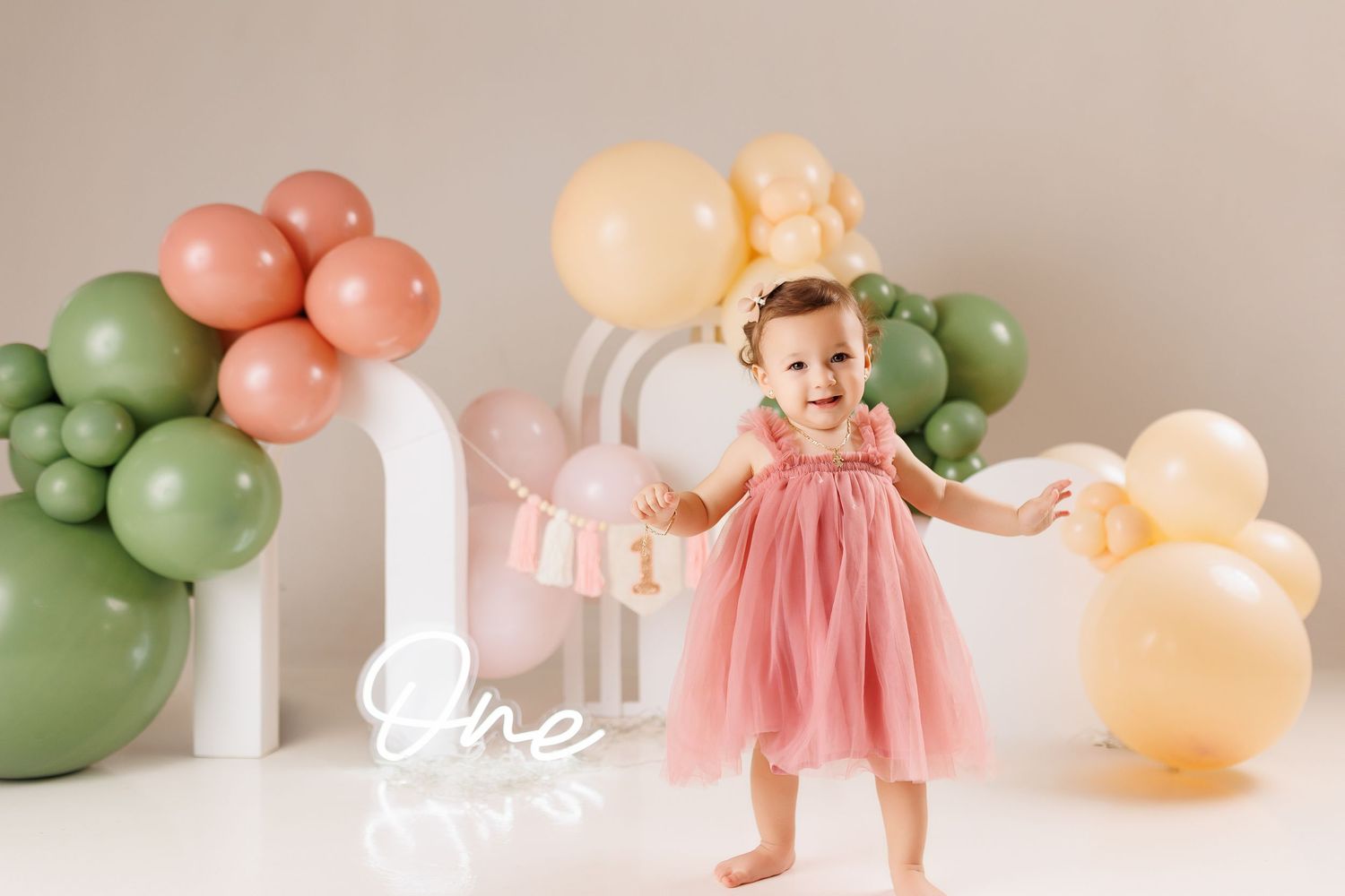 Colorful balloon arch display with sage green, peach and cream balloons decorating a white studio space.