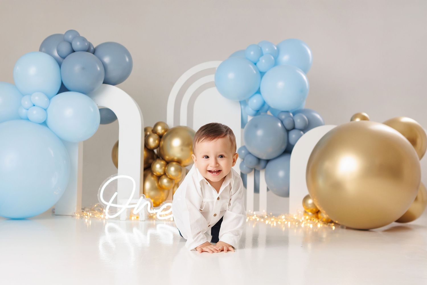 Blue and gold balloon decorations create an elegant cake smash photo setup with soft lighting and festive atmosphere.