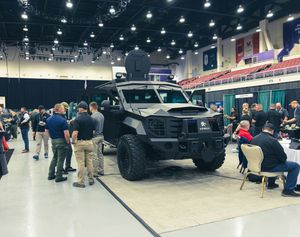 Large indoor event space with black vehicles on display and attendees walking around.