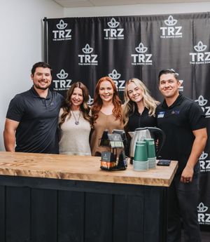 Group photo at promotional event with TRZ branded backdrop and wooden counter.
