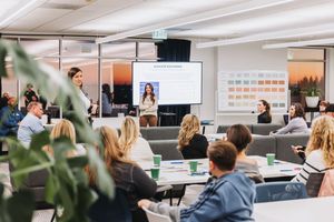 Modern conference room setting with presentation screens and attendees seated at tables.