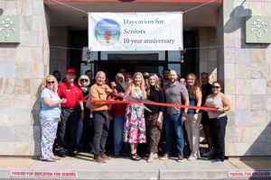Large group gathered for a ribbon cutting ceremony outside a stone building entrance.