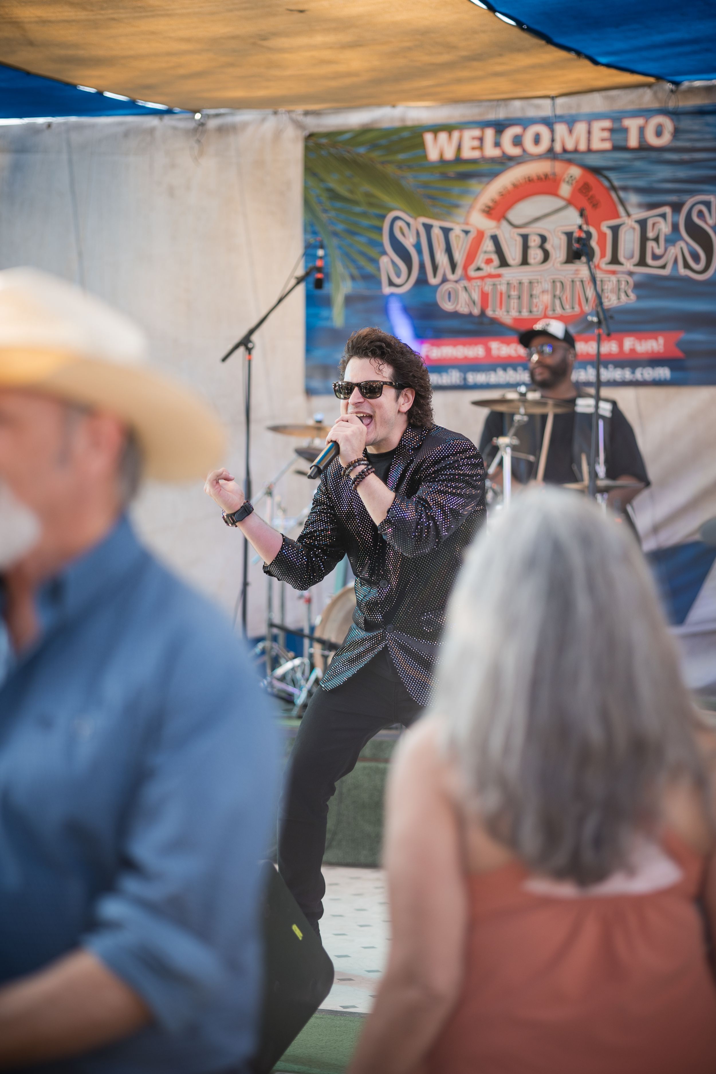 Singer performing energetically at an outdoor festival with audience members visible in background.