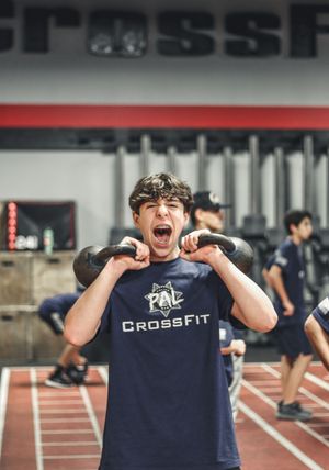 Athlete in navy CrossFit shirt celebrating enthusiastically in gym setting.