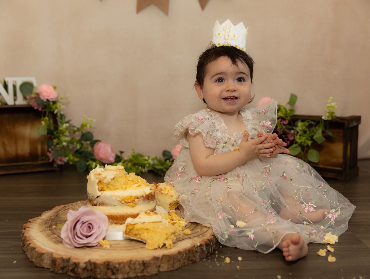 A series of cake smash photos showing a pink tulle dress and yellow frosted cake on a rustic wooden board.
