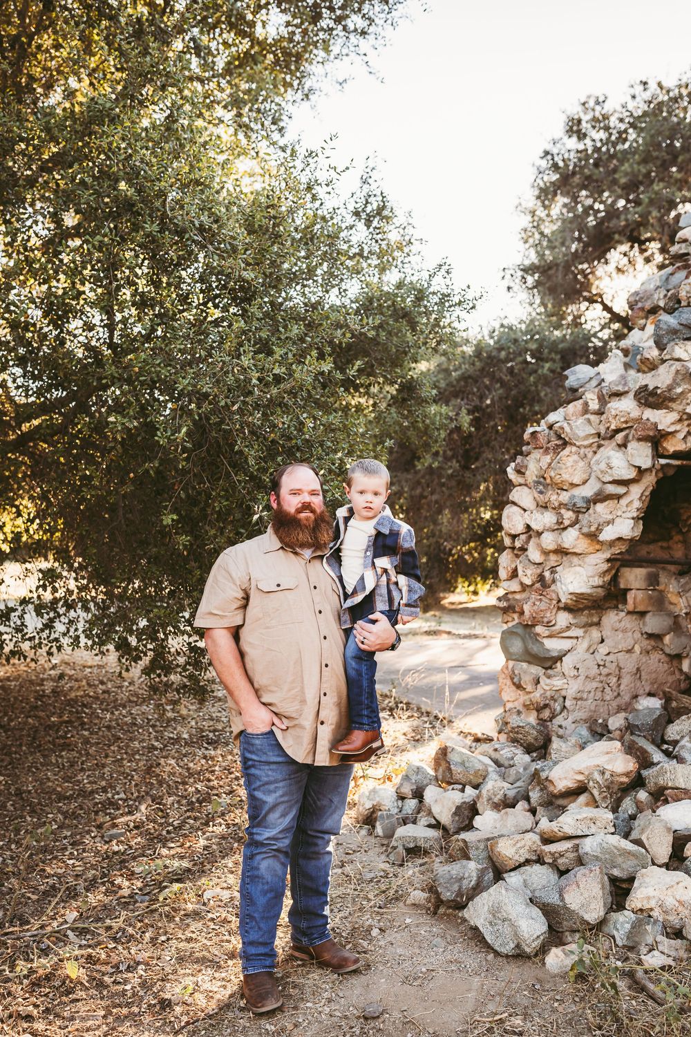 A family explores a rustic stone wall path surrounded by trees during golden hour.