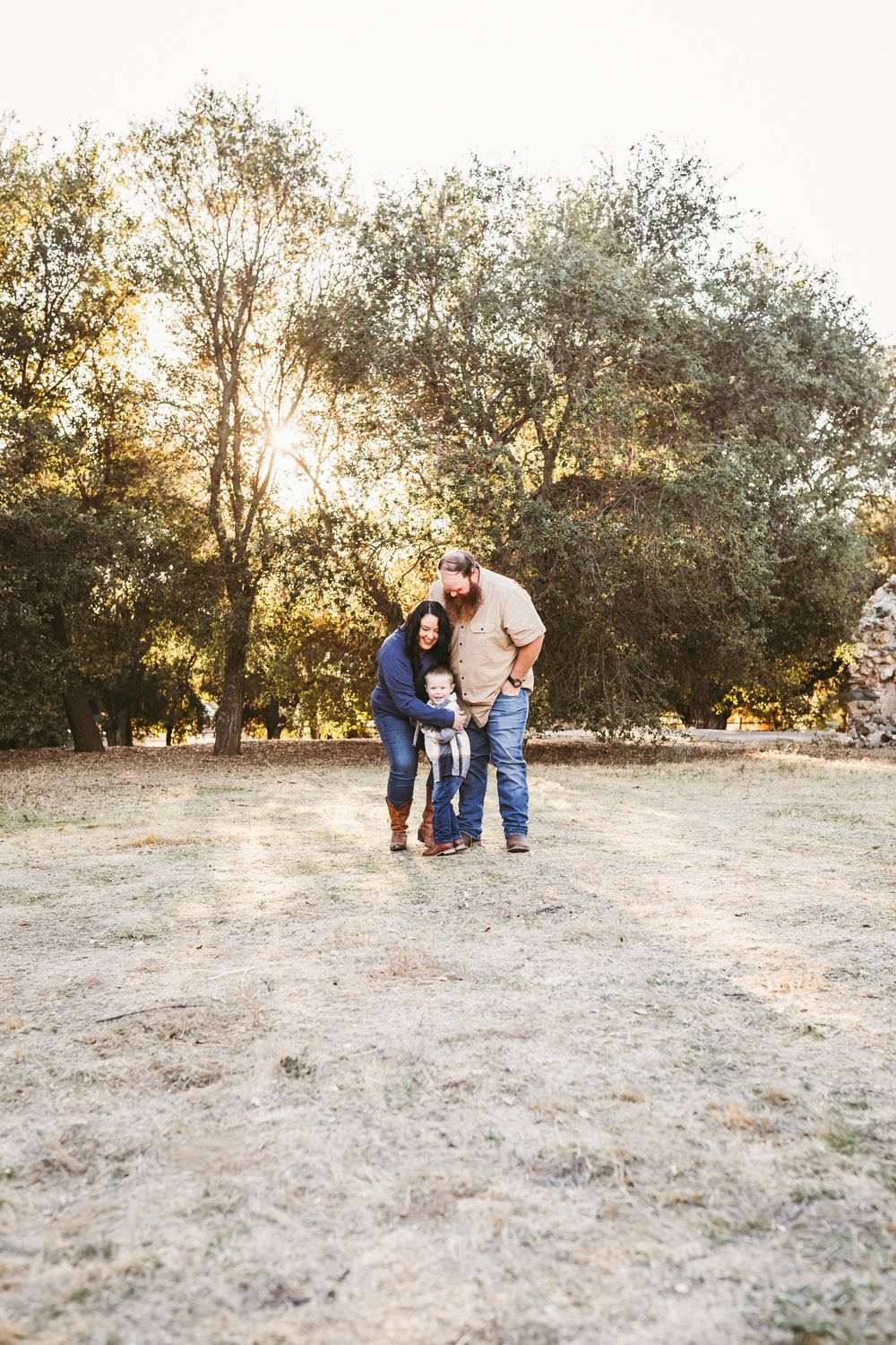 Wide angle view of a family photoshoot in a sunlit field with trees in the background.