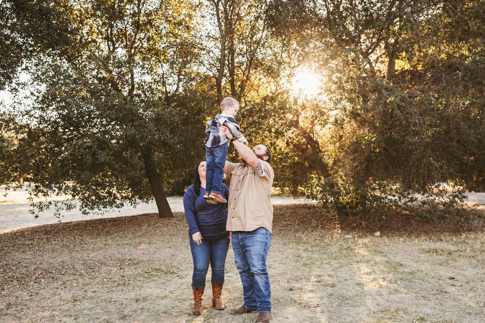 Couple shares romantic moment in golden sunlight beneath trees during outdoor autumn photo session.