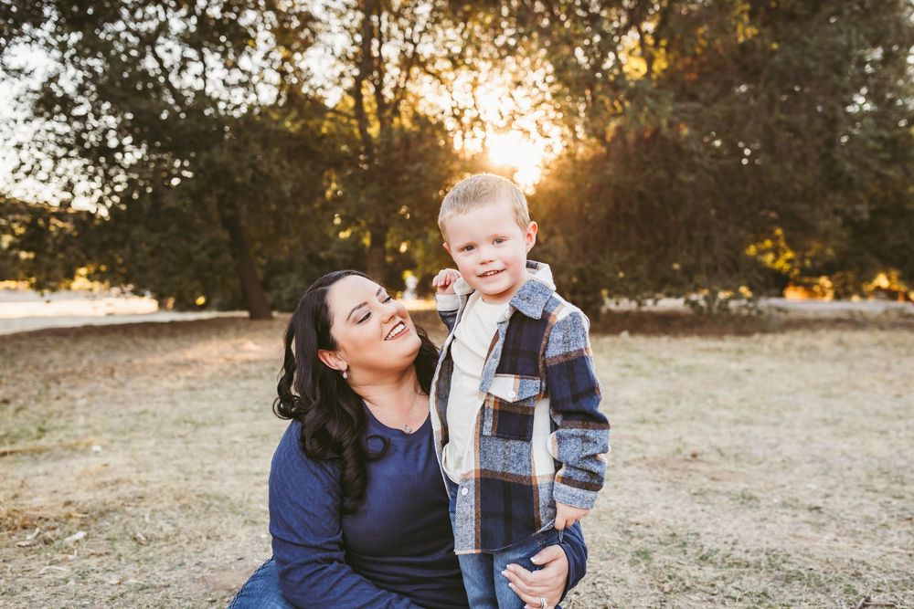 A tender family moment captured at sunset in a grassy field during a golden hour photoshoot.