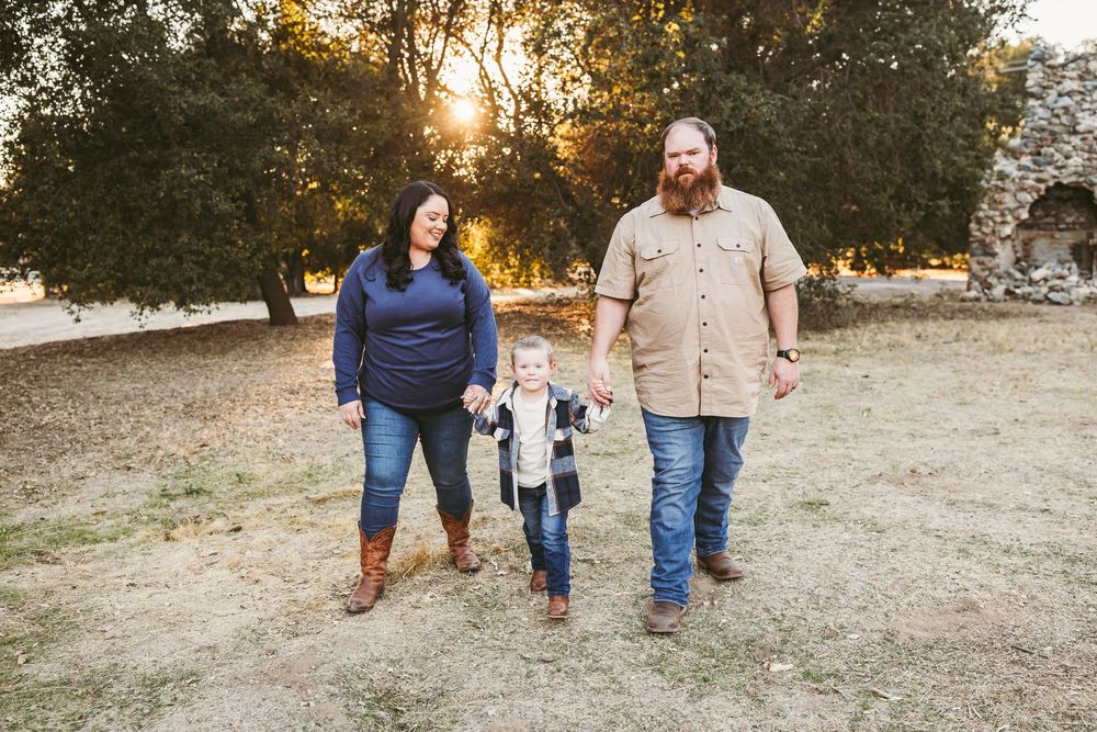 A family walks together in a grassy field during golden hour sunset while holding hands.