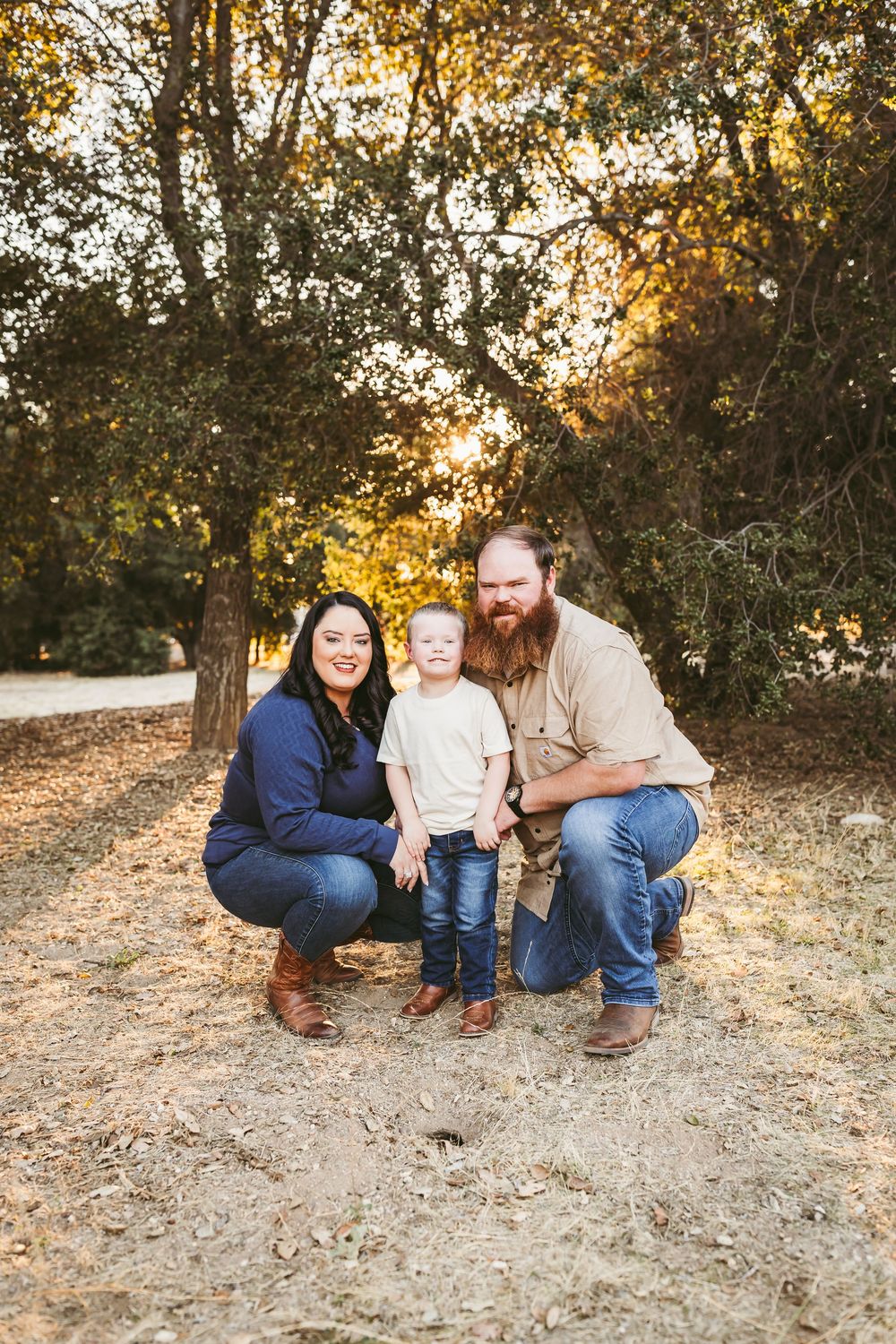 A family sits together on the ground during a golden sunset photoshoot in a natural outdoor setting.