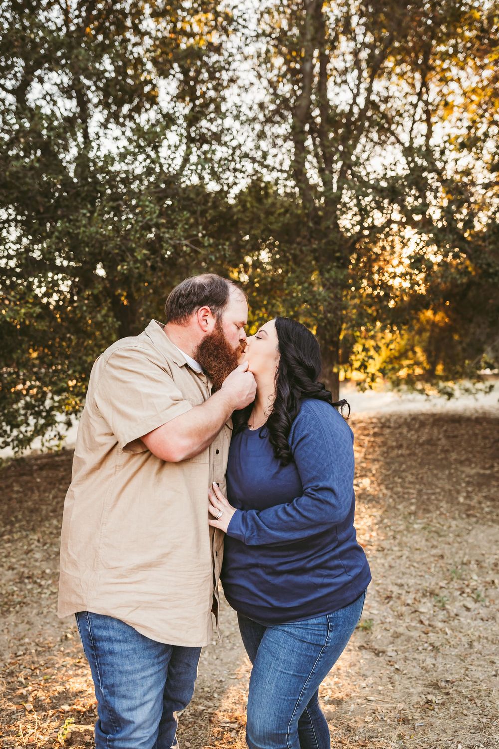 A couple in matching denim and casual wear share an intimate moment at sunset in a rustic outdoor setting.