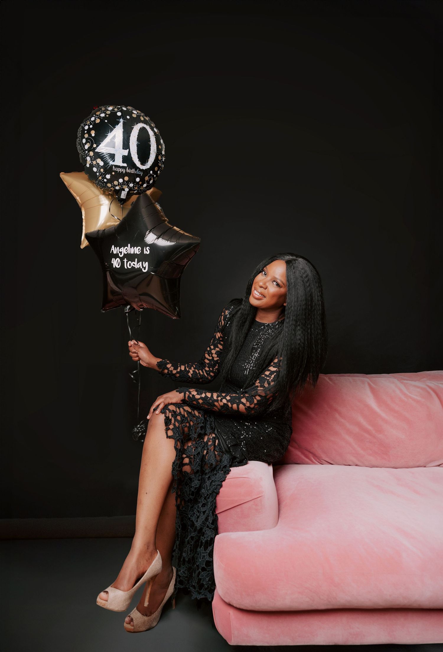 Elegant birthday celebration setup with black lace dress, pink couch, and 40th birthday balloons against dark backdrop.