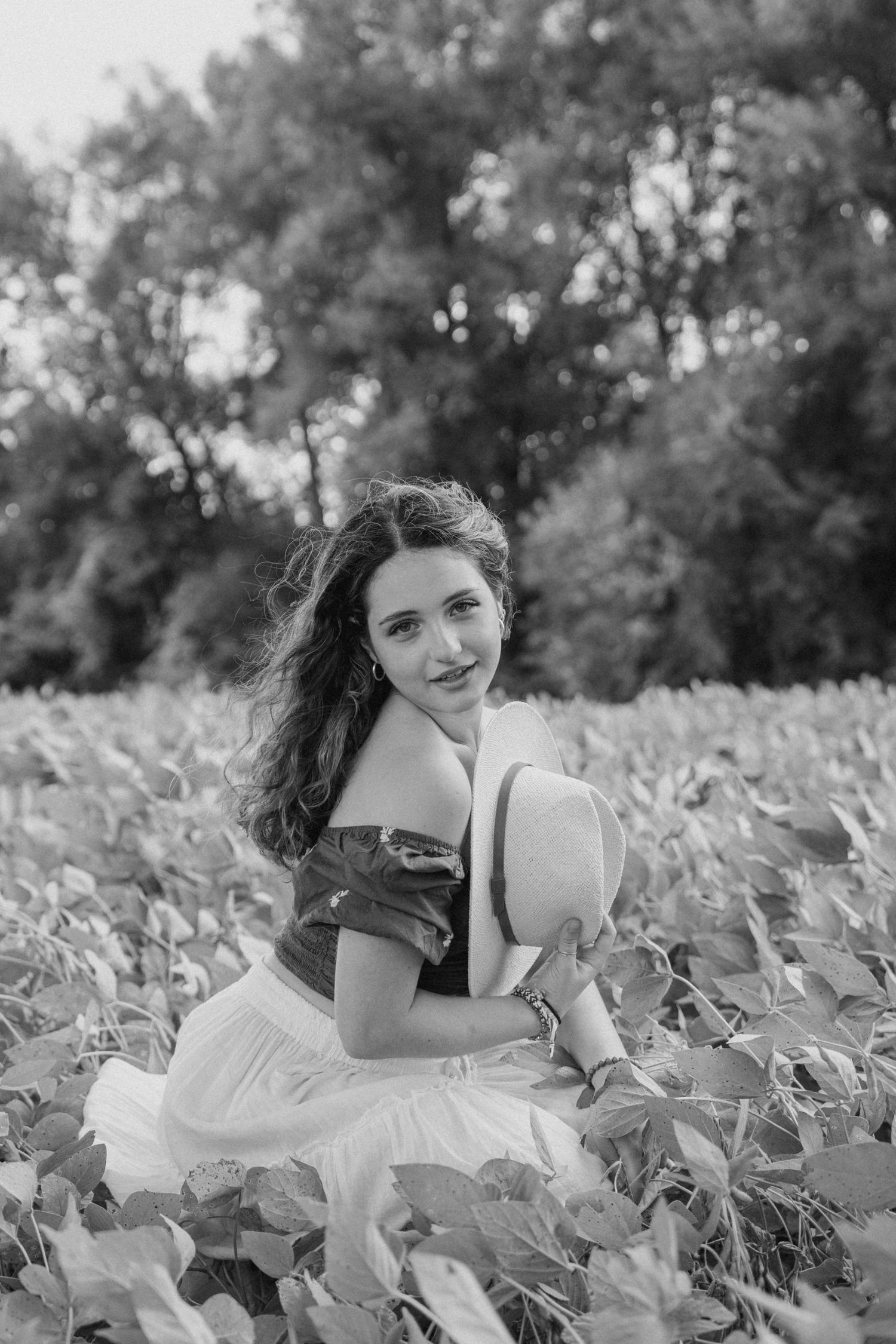A woman in a white dress lies gracefully among green leaves in a black and white outdoor portrait session.