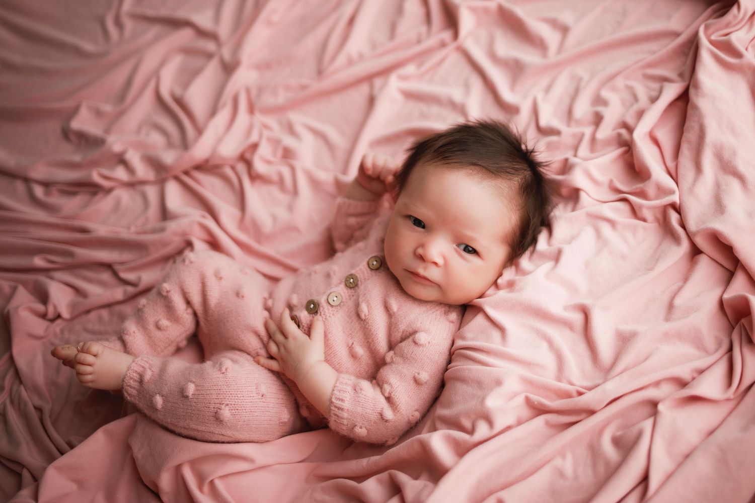 Sleeping newborn baby wrapped in soft pink blankets in a series of tender poses during a professional photo session.