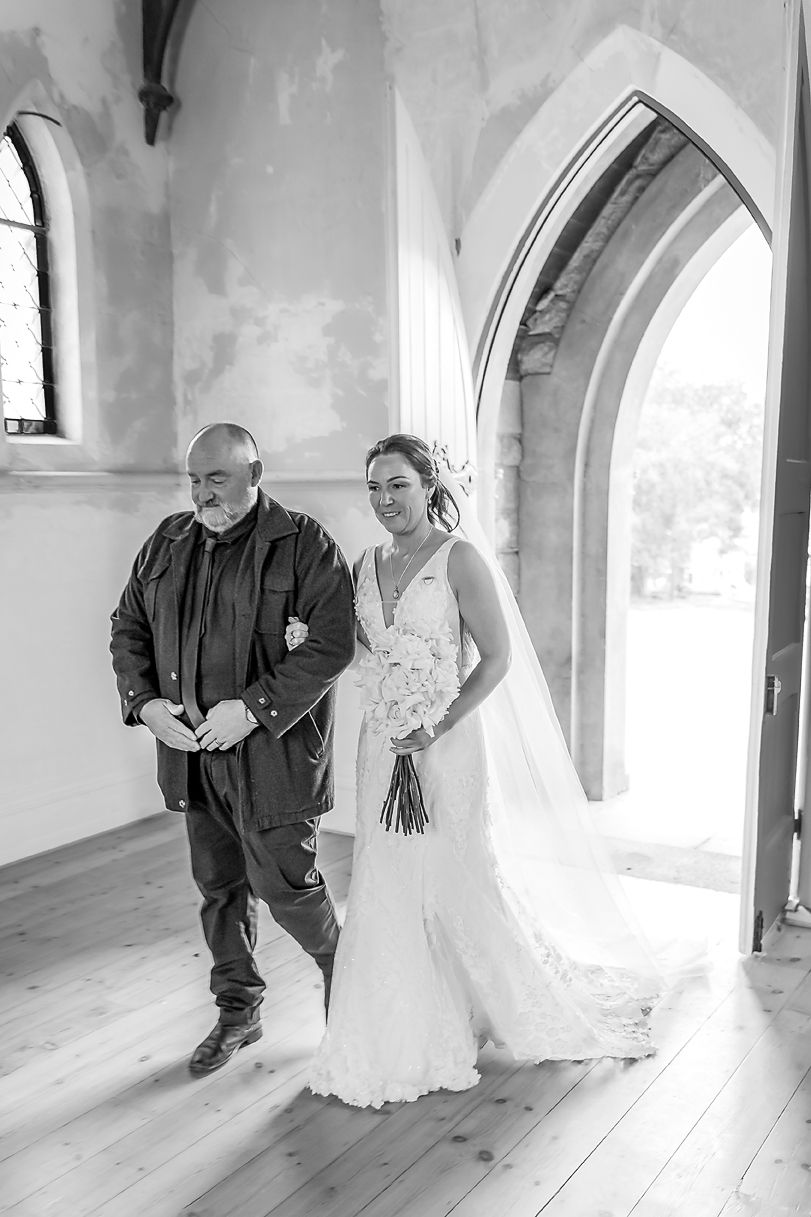 A series of four black and white photos showing a bride and father walking through an arched church hallway.