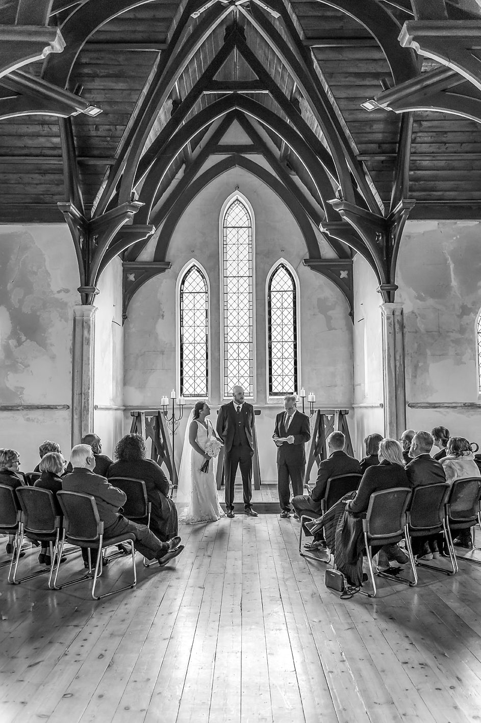 Panoramic view of a church interior with vaulted wooden beams and rows of guests seated for a ceremony.