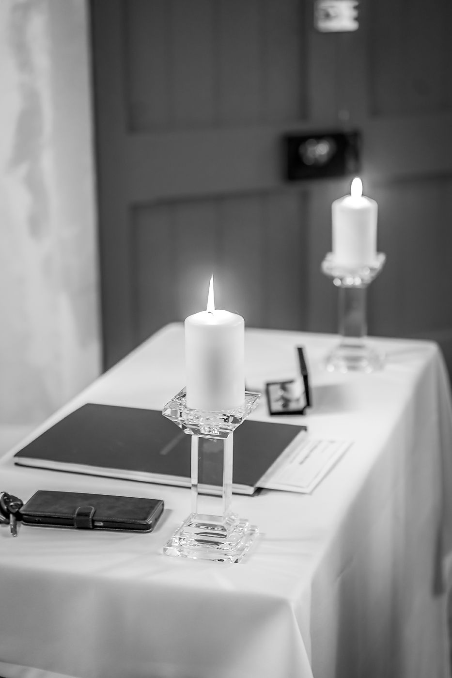 Black and white photo of lit candles and documents on a white tablecloth in a formal setting.